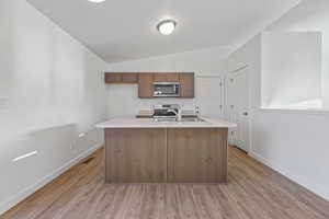 Kitchen featuring a center island with sink, light hardwood / wood-style floors, stainless steel appliances, and vaulted ceiling