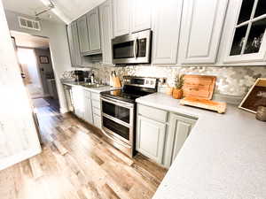 Kitchen with rail lighting, sink, appliances with stainless steel finishes, tasteful backsplash, and light hardwood / wood-style floors