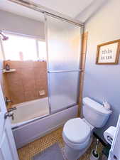 Bathroom featuring tile patterned floors, enclosed tub / shower combo, and toilet