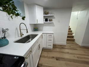 Kitchen with white cabinets, sink, decorative backsplash, light stone countertops, and light wood-type flooring