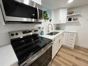 Kitchen with tasteful backsplash, stainless steel appliances, sink, light hardwood / wood-style floors, and white cabinetry