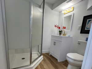 Bathroom featuring a shower with door, vanity, wood-type flooring, and toilet