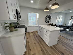 Kitchen with hardwood / wood-style floors, white cabinets, hanging light fixtures, and a kitchen island