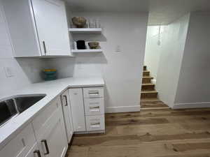 Kitchen with white cabinets, light wood-type flooring, sink, and backsplash