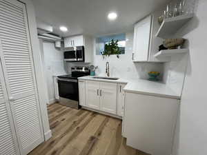 Kitchen with sink, light hardwood / wood-style flooring, tasteful backsplash, white cabinetry, and stainless steel appliances