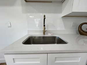 Room details with backsplash, light stone countertops, white cabinetry, and sink