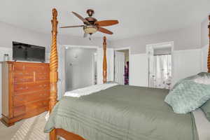 Bedroom featuring ceiling fan, light carpet, and ensuite bath