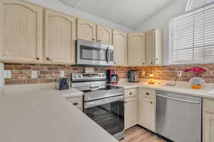 Kitchen featuring light brown cabinets, lofted ceiling, stainless steel appliances, and light hardwood / wood-style flooring