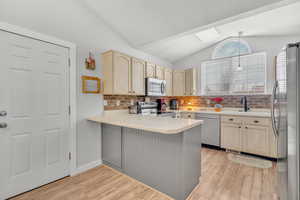 Kitchen with sink, stainless steel appliances, tasteful backsplash, kitchen peninsula, and lofted ceiling