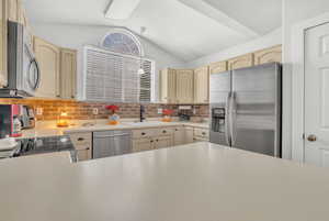 Kitchen featuring light brown cabinets, lofted ceiling, sink, appliances with stainless steel finishes, and tasteful backsplash