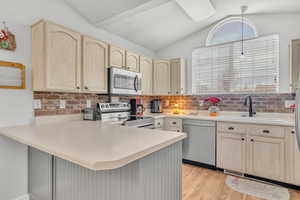 Kitchen featuring sink, vaulted ceiling, light wood-type flooring, appliances with stainless steel finishes, and kitchen peninsula