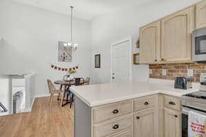 Kitchen featuring backsplash, an inviting chandelier, light brown cabinetry, decorative light fixtures, and stainless steel appliances