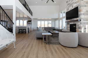 Living room featuring a stone fireplace, light wood-type flooring, a towering ceiling, and a wealth of natural light