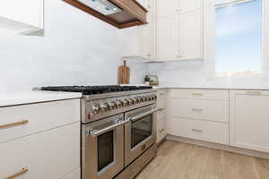 Kitchen with backsplash, extractor fan, double oven range, white cabinets, and light hardwood / wood-style floors