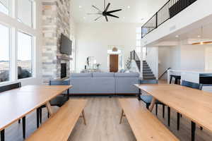 Living room with ceiling fan, light wood-type flooring, a fireplace, and a high ceiling