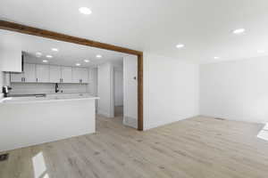 Kitchen with kitchen peninsula, stove, sink, white cabinets, and light hardwood / wood-style floors