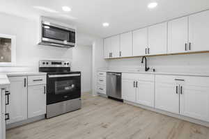 Kitchen with sink, white cabinetry, stainless steel appliances, and light hardwood / wood-style flooring