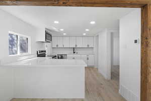 Kitchen featuring kitchen peninsula, appliances with stainless steel finishes, light wood-type flooring, sink, and white cabinets