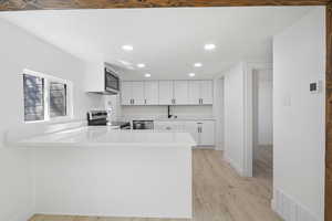 Kitchen featuring kitchen peninsula, appliances with stainless steel finishes, light wood-type flooring, sink, and white cabinets