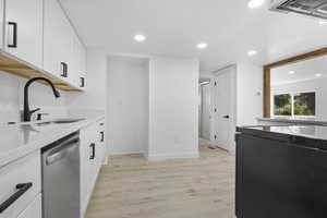 Kitchen with stainless steel dishwasher, white cabinets, sink, and light hardwood / wood-style flooring