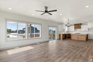 Unfurnished living room featuring sink, light hardwood / wood-style floors, and ceiling fan with notable chandelier