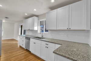 Kitchen with decorative backsplash, appliances with stainless steel finishes, light wood-type flooring, sink, and white cabinetry