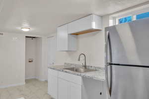 Kitchen with stainless steel refrigerator, sink, white cabinets, and a textured ceiling