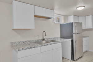 Kitchen with white cabinets, a textured ceiling, stainless steel refrigerator, and sink