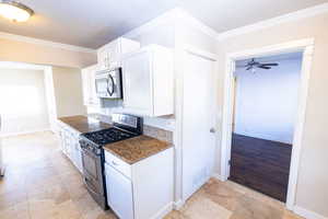 Kitchen with stainless steel appliances, white cabinetry, ornamental molding, and dark stone countertops