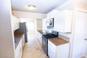 Kitchen featuring white cabinets, stainless steel appliances, crown molding, and dark stone counters