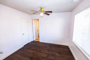 Empty room featuring a textured ceiling, ceiling fan, dark wood-type flooring, and a wealth of natural light