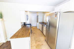 Kitchen with appliances with stainless steel finishes, dark stone counters, sink, light hardwood / wood-style flooring, and white cabinetry