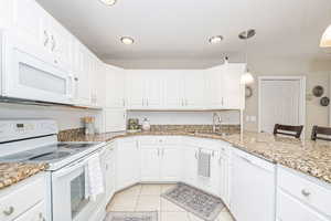 Kitchen featuring granite countertop, white appliances, sink, pendant lighting, white cabinetry, and a breakfast bar area