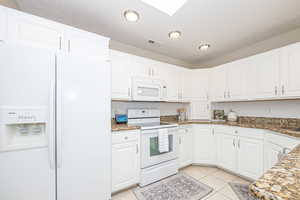 Kitchen featuring white cabinets, granite stone countertops, a textured ceiling, white appliances, and light tile patterned floors