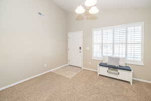 Carpeted foyer entrance featuring lofted ceiling and an inviting chandelier