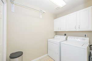 Laundry area featuring light tile patterned floors, cabinets, a textured ceiling, and washer and dryer, clothes hanging rack, and pantry