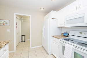 Kitchen, entry to pantry/laundry room featuring light granite , white appliances, a textured ceiling, light tile patterned floors, and white cabinetry