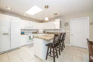 Kitchen with granite countertop, white cabinets, white appliances, a skylight, and light stone countertops