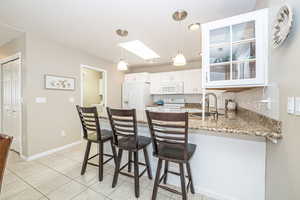 Kitchen with white cabinets, granite countertop, a kitchen bar, white appliances, and a skylight