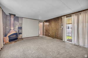 Unfurnished living room with a wood stove, wooden walls, carpet floors, and a textured ceiling