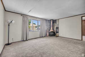 Unfurnished living room with a wood stove, carpet floors, a textured ceiling, and ornamental molding