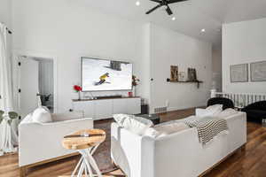 Living room with dark wood-type flooring, ceiling fan, and high vaulted ceiling