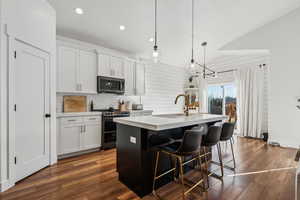 Kitchen with hanging light fixtures, appliances with stainless steel finishes, a kitchen island with sink, and white cabinets