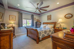 Primary Owner Suite / Bedroom with a raised ceiling, ceiling fan, light carpet, and a textured ceiling