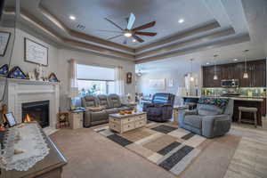 Living room with a raised ceiling, ceiling fan, a fireplace, and light hardwood / wood-style flooring