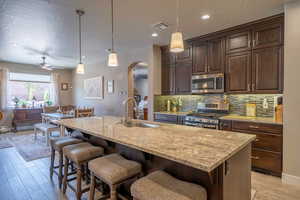 Kitchen featuring light stone countertops, sink, hanging light fixtures, stainless steel appliances, and a center island with sink