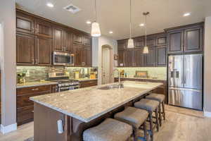 Kitchen featuring appliances with stainless steel finishes, light wood-type flooring, dark brown cabinetry, sink, and hanging light fixtures