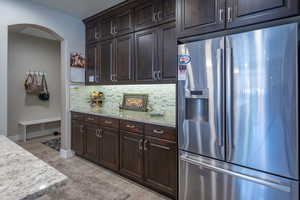 Kitchen featuring light hardwood / wood-style floors, light stone counters, stainless steel refrigerator with ice dispenser, and tasteful backsplash