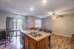 Kitchen with a kitchen island with sink, sink, decorative light fixtures, hardwood / wood-style flooring, and dishwasher