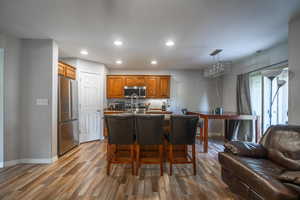 Kitchen featuring stainless steel appliances, decorative light fixtures, a center island with sink, hardwood / wood-style floors, and a breakfast bar area